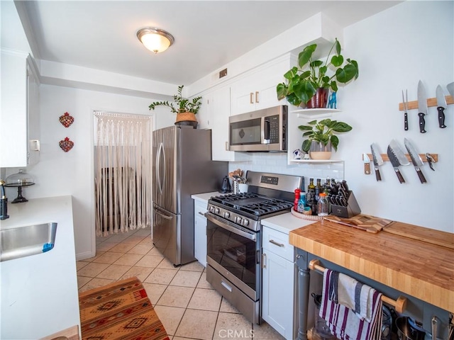 kitchen with light tile patterned floors, a sink, white cabinetry, appliances with stainless steel finishes, and tasteful backsplash