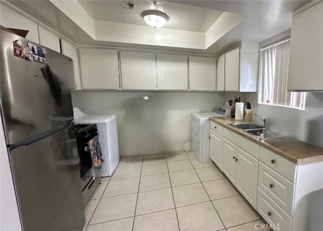 kitchen with light tile patterned floors, a tray ceiling, a sink, and freestanding refrigerator