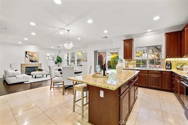 kitchen with light stone counters, decorative backsplash, crown molding, and a tile fireplace