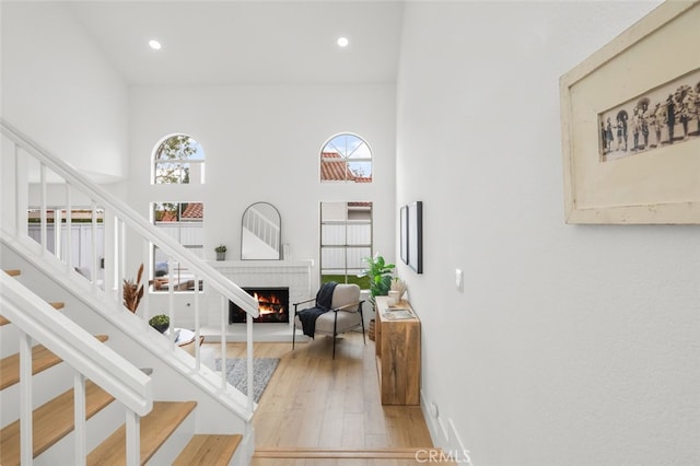 interior space featuring a warm lit fireplace, stairway, recessed lighting, and light wood-style floors