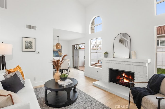 living room featuring light wood-style floors, baseboards, a fireplace, and visible vents