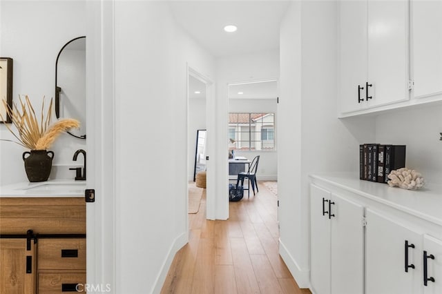 hallway with light wood-type flooring, a sink, baseboards, and recessed lighting