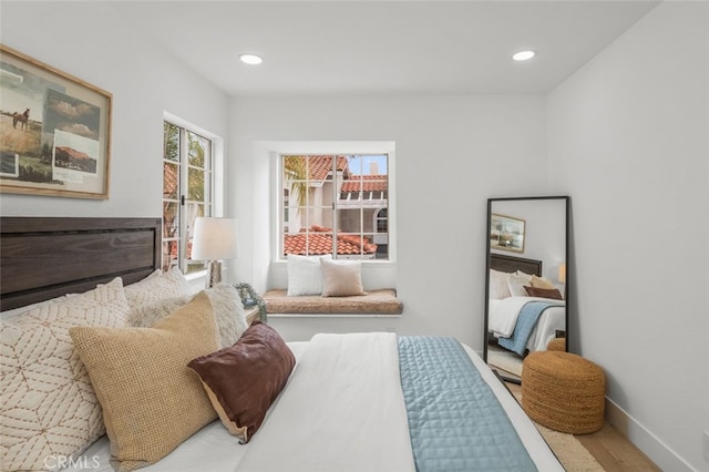 bedroom featuring recessed lighting, a glass covered fireplace, baseboards, and wood finished floors