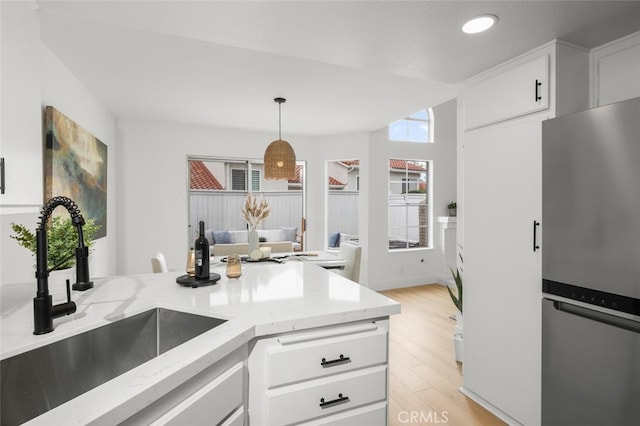 kitchen featuring light wood finished floors, freestanding refrigerator, white cabinetry, a sink, and light stone countertops