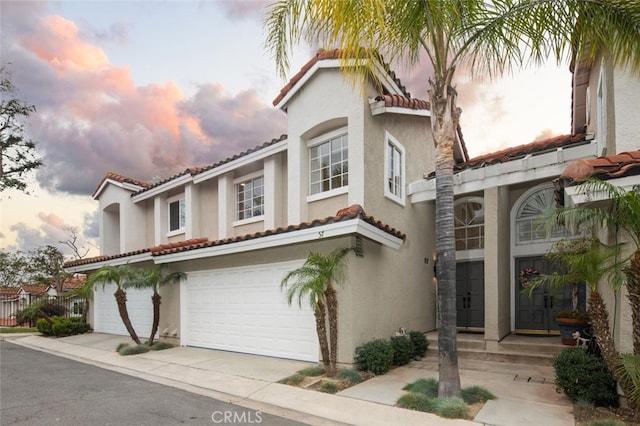 mediterranean / spanish-style home featuring a tile roof, driveway, an attached garage, and stucco siding