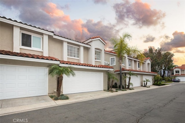 mediterranean / spanish-style home with a garage, a tiled roof, concrete driveway, and stucco siding