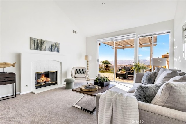 carpeted living area featuring visible vents, baseboards, high vaulted ceiling, and a glass covered fireplace