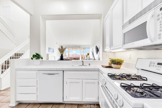 kitchen with white cabinets, white appliances, tile countertops, and a sink