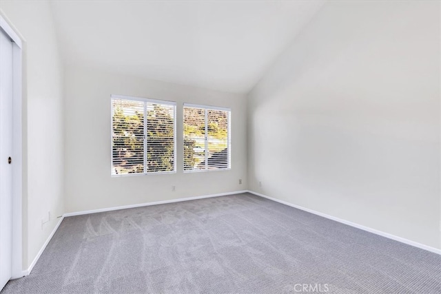 carpeted empty room with vaulted ceiling and baseboards