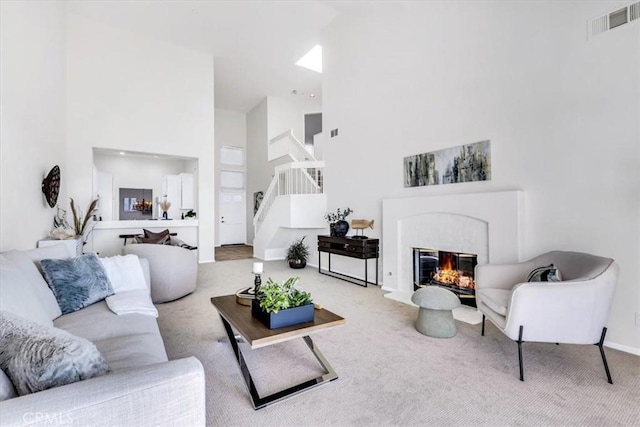 carpeted living room featuring baseboards, visible vents, a high ceiling, stairs, and a glass covered fireplace