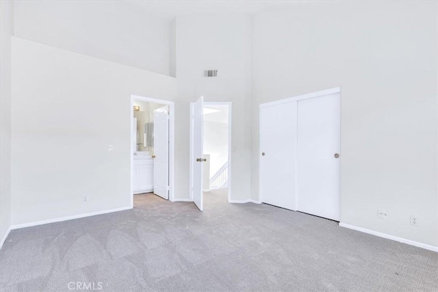 unfurnished bedroom with a closet, visible vents, a high ceiling, and carpet