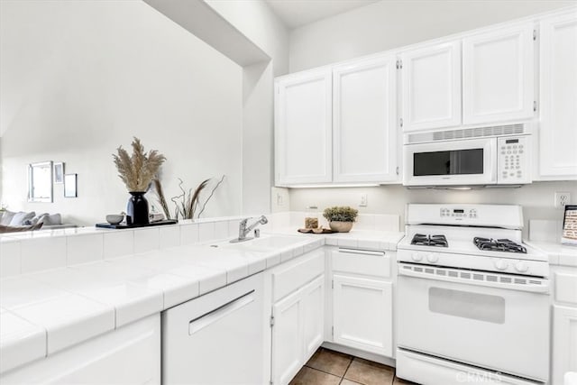 kitchen with white appliances, a sink, tile counters, white cabinets, and tile patterned floors