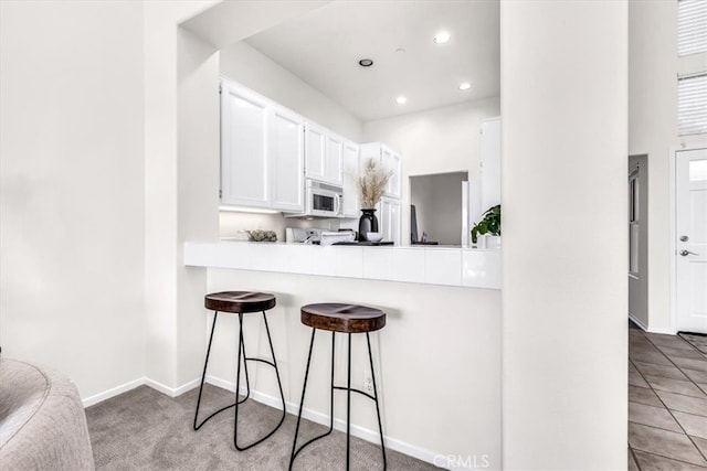 kitchen featuring white microwave, recessed lighting, light countertops, white cabinets, and a kitchen breakfast bar