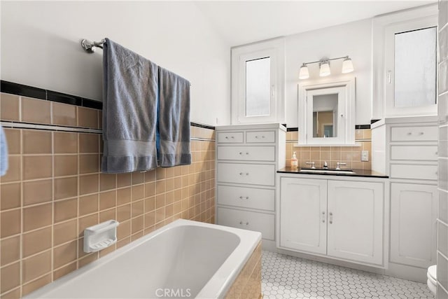 bathroom featuring tiled bath, toilet, tile patterned floors, vanity, and tile walls