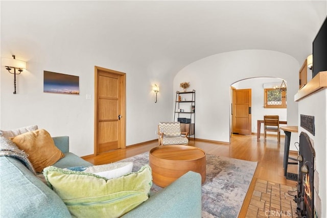 living room with arched walkways, vaulted ceiling, light wood finished floors, and baseboards