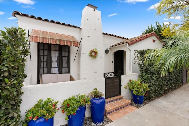 view of front facade with a tiled roof, a chimney, and stucco siding