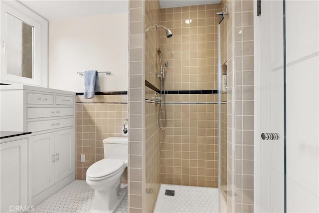 bathroom featuring toilet, a shower stall, tile walls, and tile patterned floors