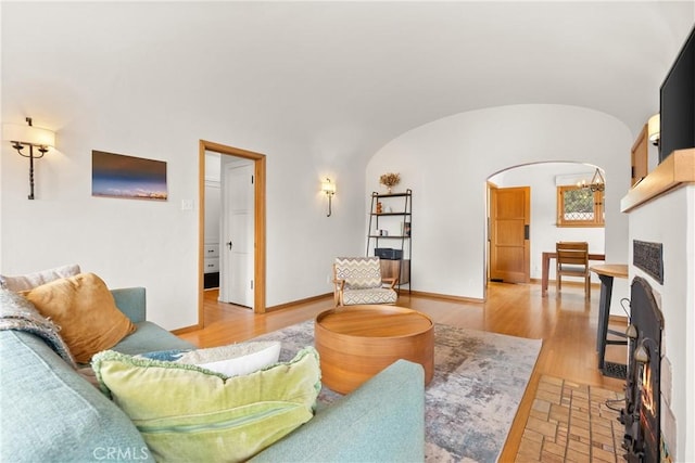 living area with arched walkways, light wood finished floors, lofted ceiling, and baseboards