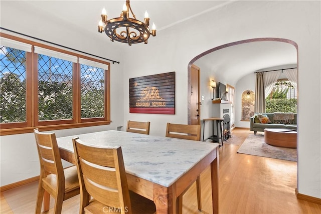 dining space featuring baseboards, a fireplace, arched walkways, and wood finished floors