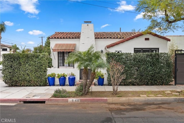 mediterranean / spanish home featuring a tiled roof, a chimney, and stucco siding