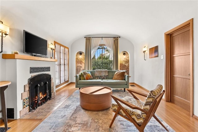 living room featuring lofted ceiling, baseboards, a tiled fireplace, and light wood finished floors