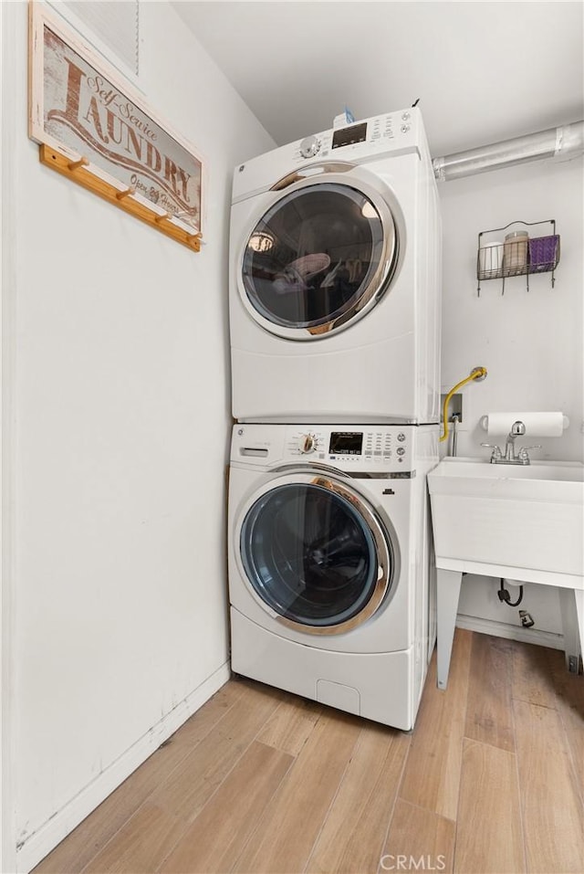 laundry room featuring stacked washing maching and dryer, laundry area, light wood finished floors, and a sink