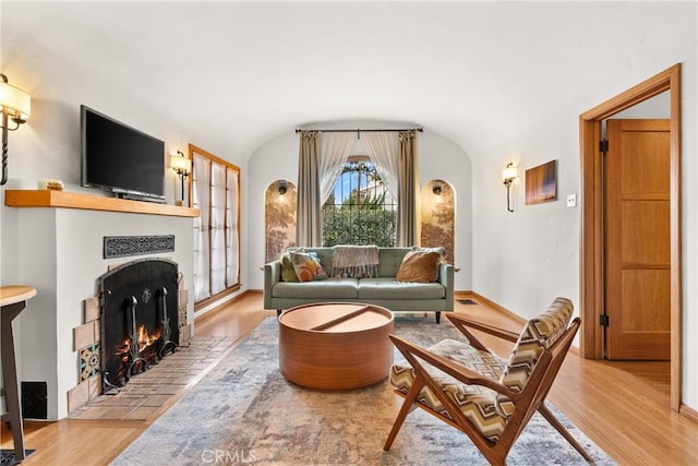 living area featuring a fireplace, lofted ceiling, visible vents, light wood-type flooring, and baseboards