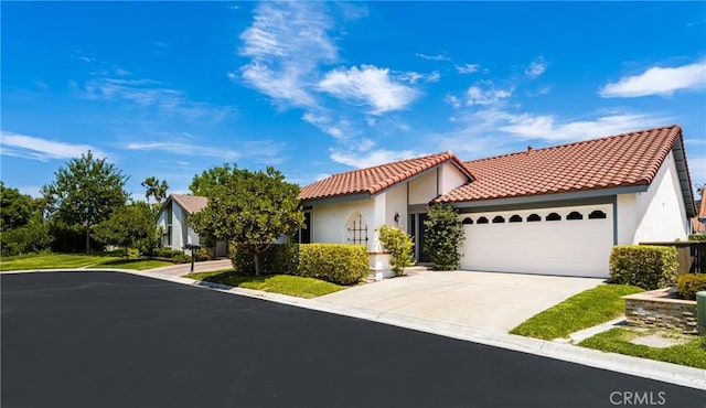 mediterranean / spanish-style home featuring an attached garage, a tile roof, concrete driveway, and stucco siding