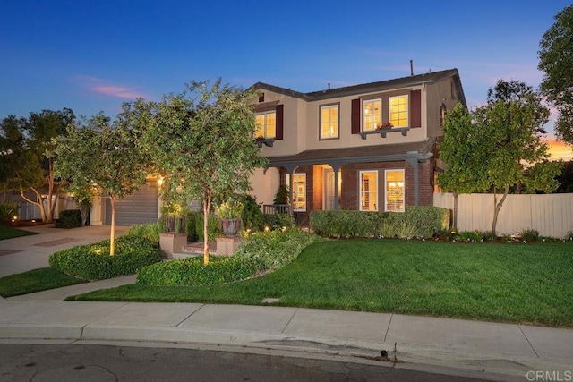 traditional-style home with an attached garage, fence, driveway, a lawn, and stucco siding