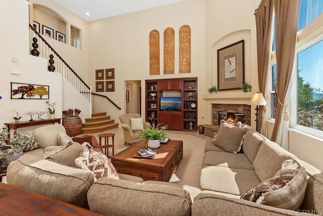 living area with stairs, carpet floors, a stone fireplace, and a towering ceiling