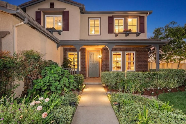 property entrance with stucco siding, fence, a porch, and brick siding