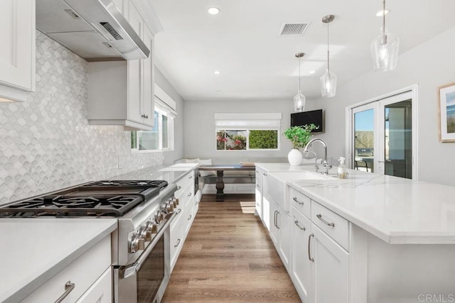 kitchen with visible vents, custom range hood, backsplash, a sink, and high end range