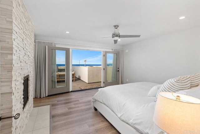 bedroom with access to outside, a stone fireplace, wood finished floors, and recessed lighting