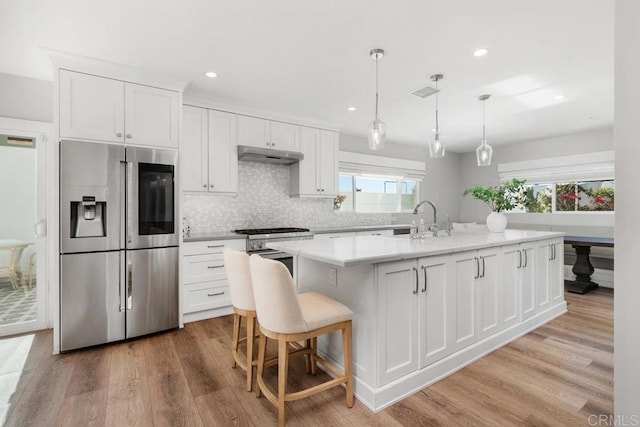 kitchen with under cabinet range hood, white cabinetry, appliances with stainless steel finishes, and light wood-style flooring