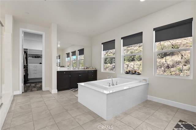 full bath with a spacious closet, a garden tub, vanity, and tile patterned floors