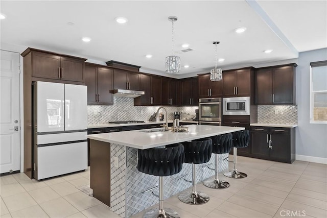 kitchen with light countertops, appliances with stainless steel finishes, a sink, under cabinet range hood, and a kitchen breakfast bar