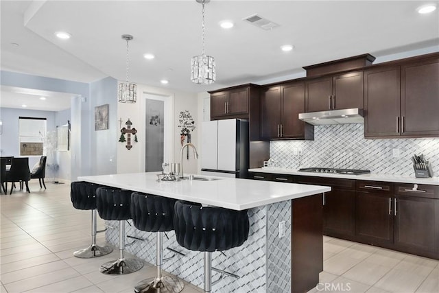 kitchen with a breakfast bar, visible vents, freestanding refrigerator, a sink, and under cabinet range hood