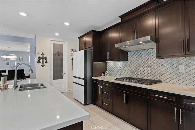 kitchen featuring under cabinet range hood, stainless steel gas cooktop, a sink, light countertops, and freestanding refrigerator