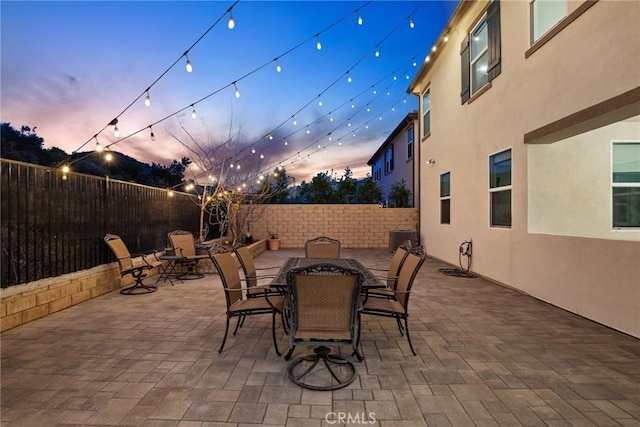 patio terrace at dusk with central air condition unit, a fenced backyard, and outdoor dining area