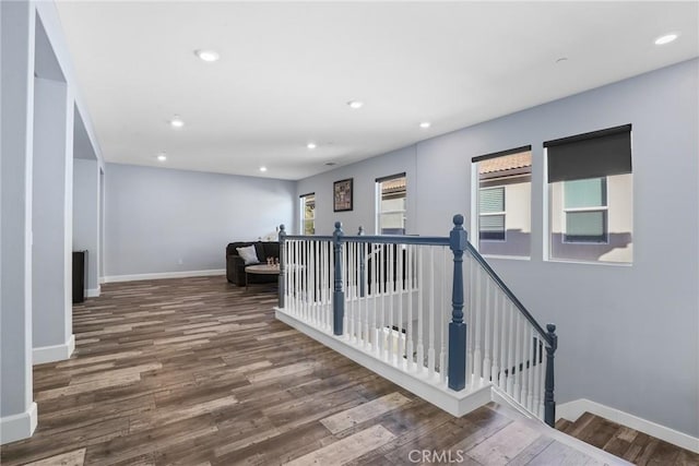 corridor with recessed lighting, baseboards, wood finished floors, and an upstairs landing