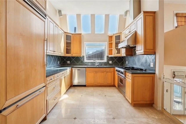 kitchen featuring dark countertops, glass insert cabinets, a sink, high quality appliances, and under cabinet range hood