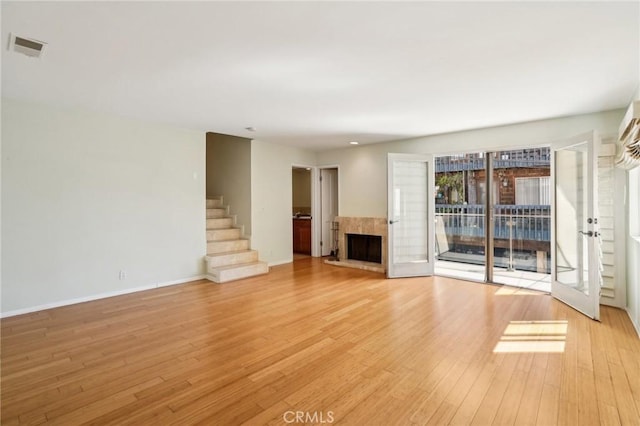 unfurnished living room with a fireplace with raised hearth, visible vents, light wood-style floors, baseboards, and stairs