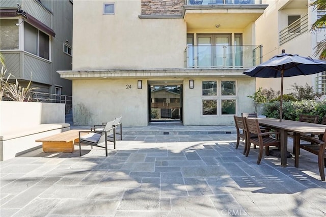 doorway to property featuring outdoor dining space, a patio area, a balcony, and stucco siding