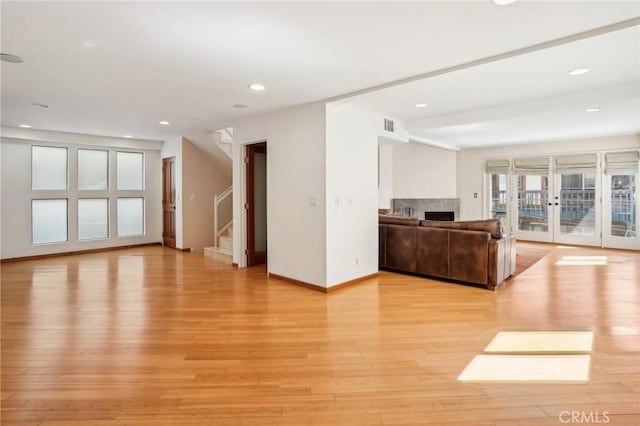 unfurnished living room with visible vents, baseboards, stairway, light wood-type flooring, and a fireplace