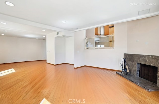 unfurnished living room with recessed lighting, a high end fireplace, wood finished floors, and baseboards