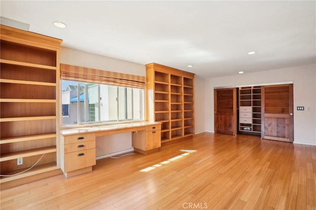 unfurnished office with baseboards, recessed lighting, light wood finished floors, and built in desk