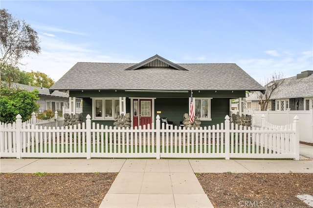 view of front facade featuring covered porch, a fenced front yard, and roof with shingles