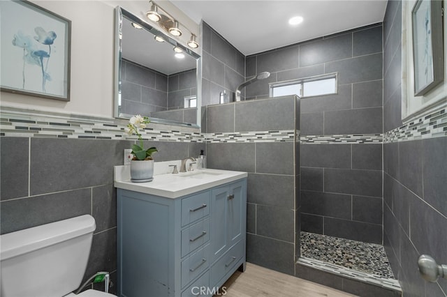 bathroom featuring tile walls, toilet, vanity, wood finished floors, and a walk in shower