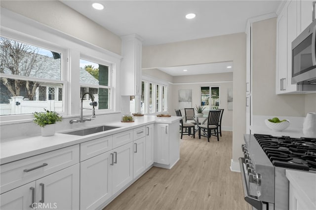 kitchen featuring stainless steel appliances, white cabinets, a sink, and light wood finished floors