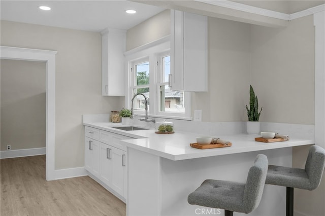 kitchen with a breakfast bar, white cabinetry, a sink, and light wood-style flooring